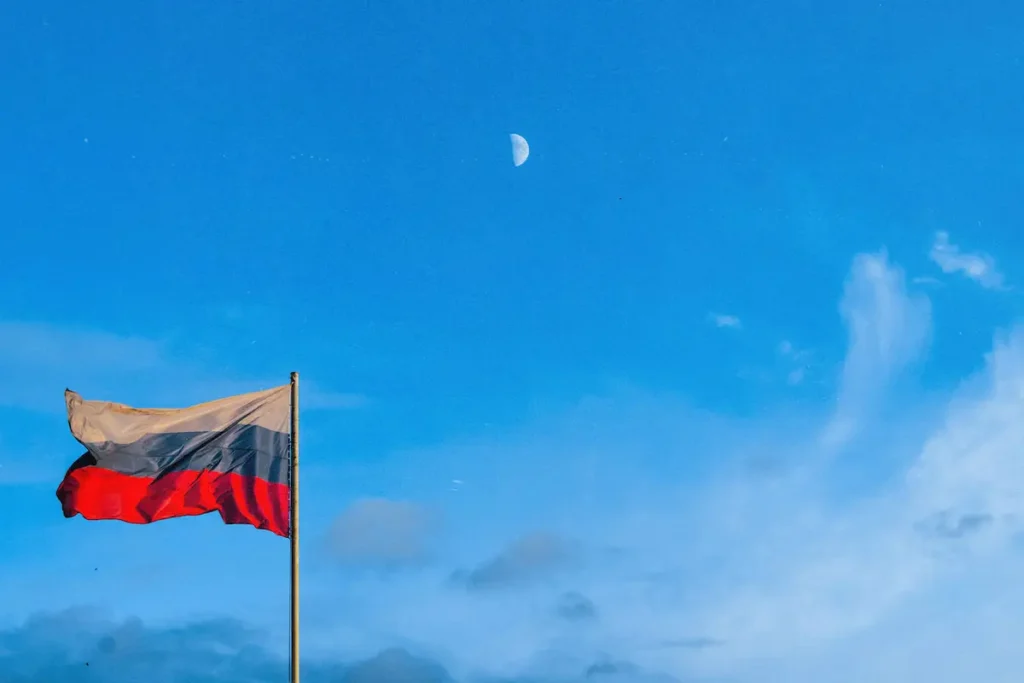 Russian flag waving against a bright blue sky with the moon visible.