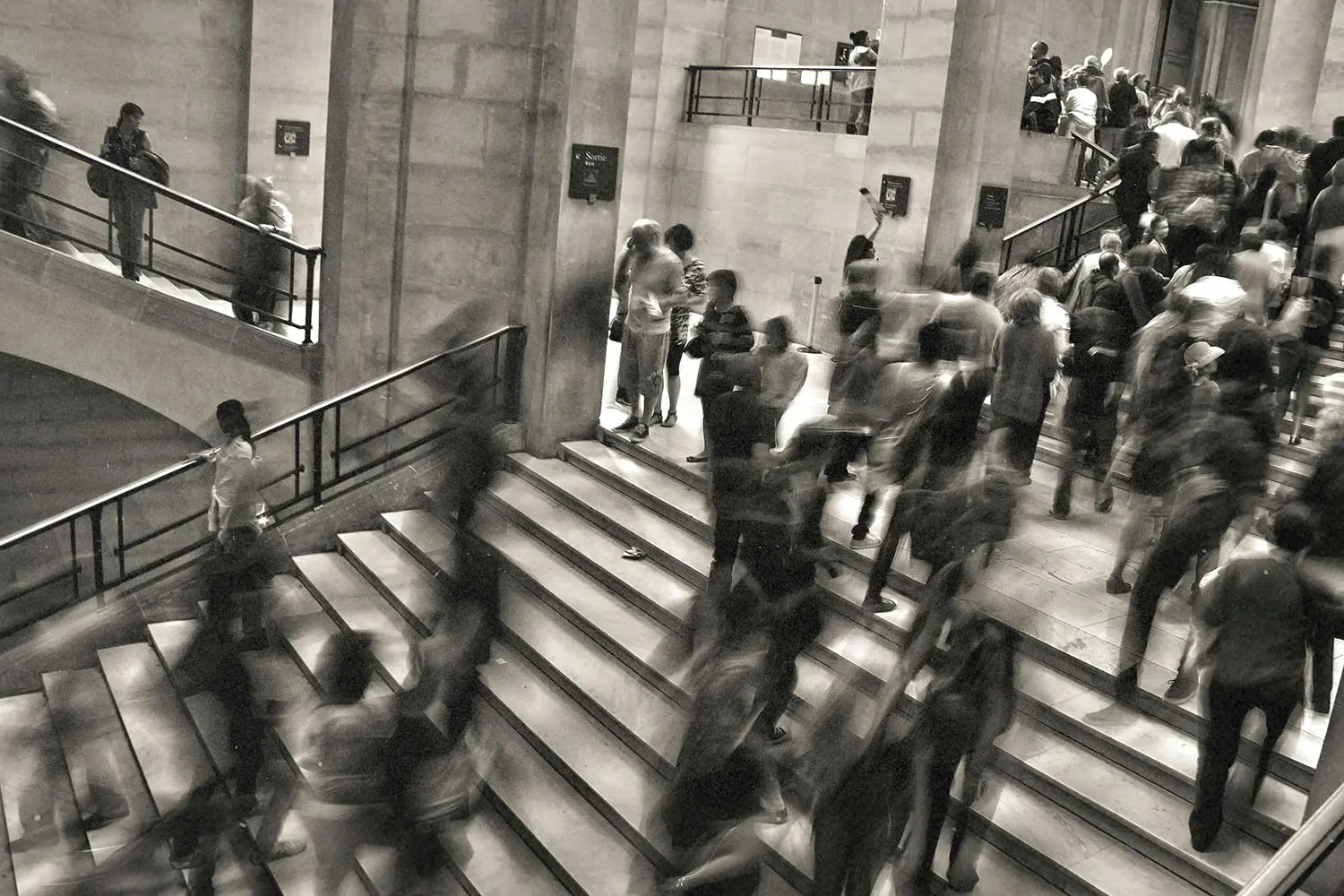 black and white photo of people walking up and down stairs in a busy scene