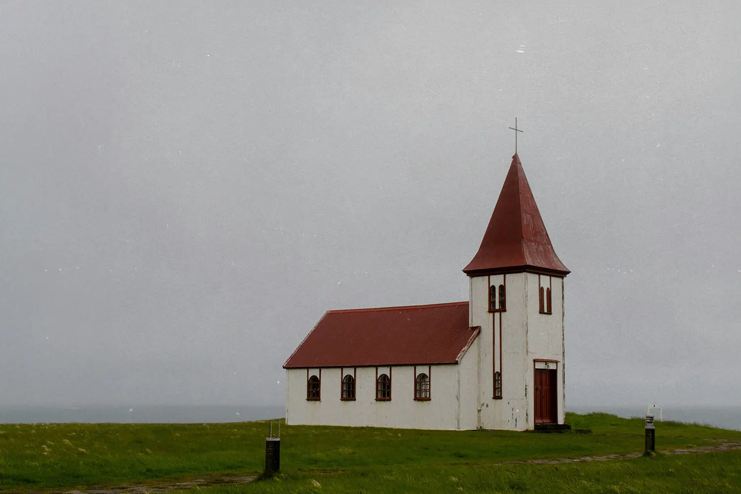 older white church with red roof in the middle of a field