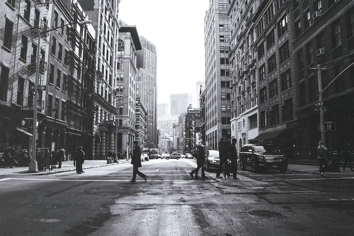 black and white photo of people walking across a crosswalk in the city