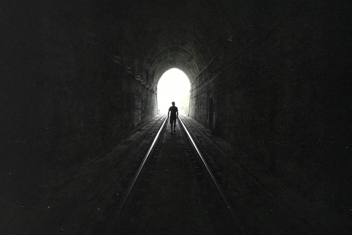 Man walking on train tracks in a tunnel towards light