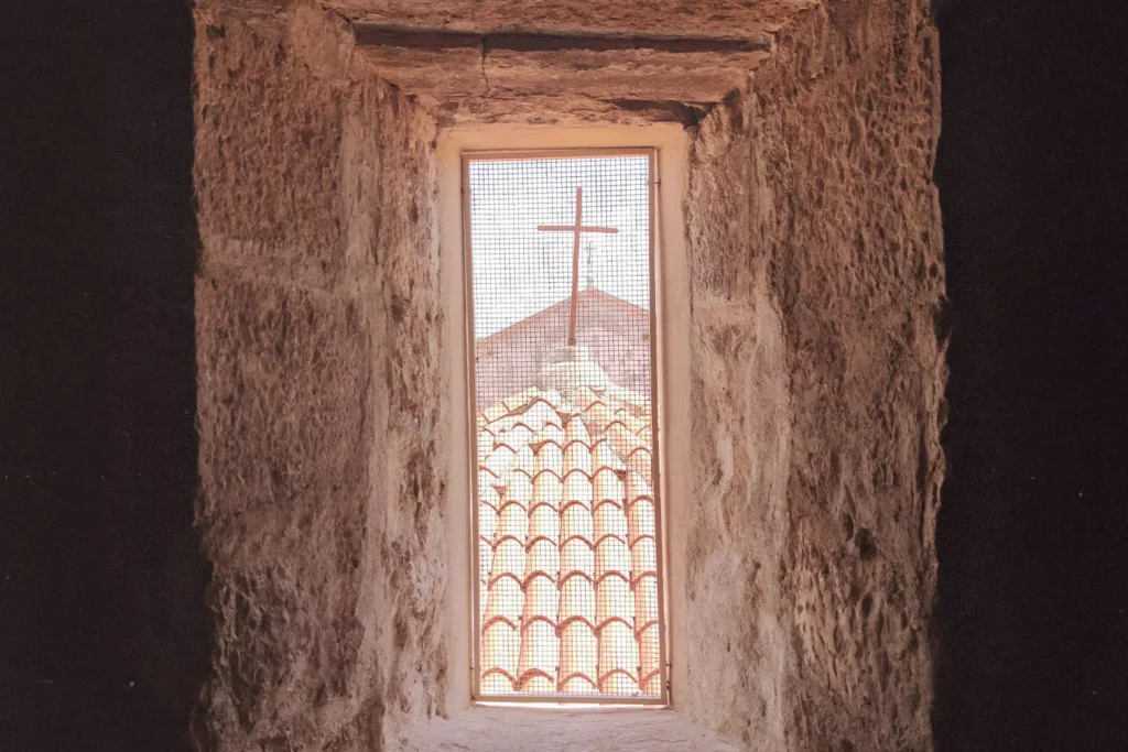 looking out of a wired window at a cross on top a building