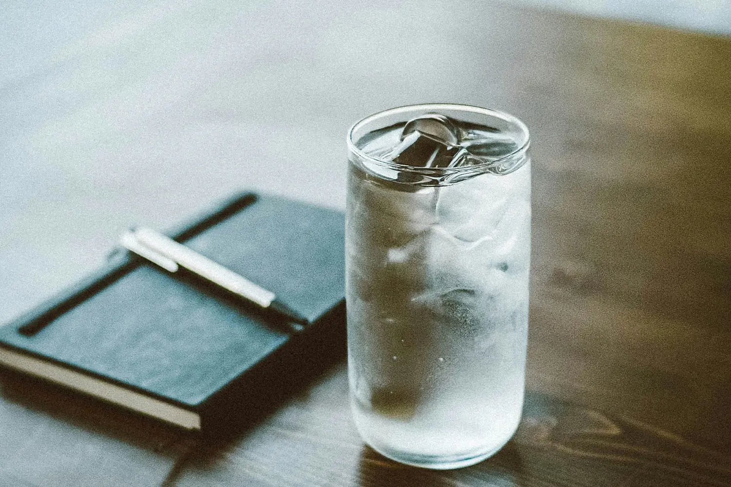 glass of iced water next to black notebook on wood table