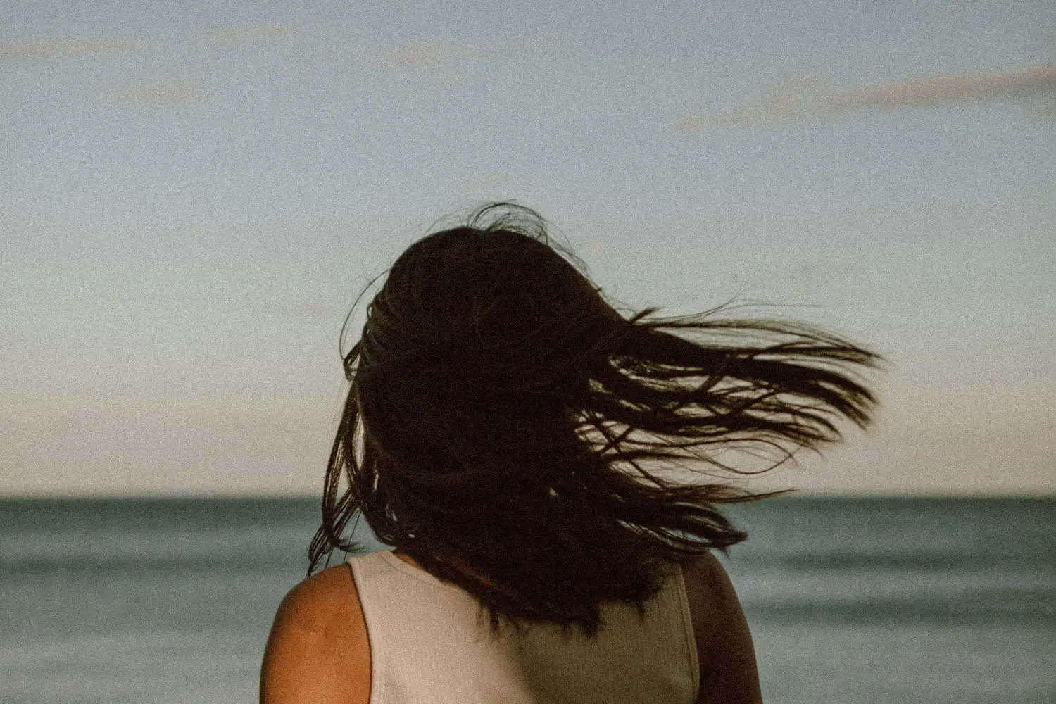 girls hair blowing in the wind as she stands in front of the ocean