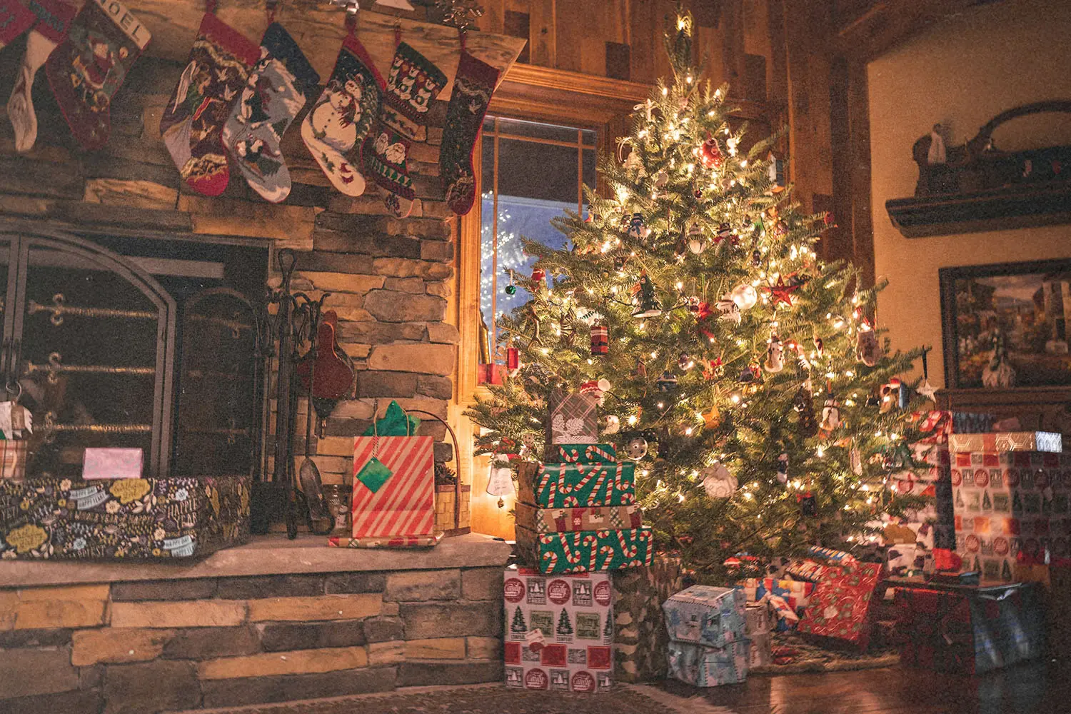 Lit Christmas tree with presents underneath and stockings hung above the fire place