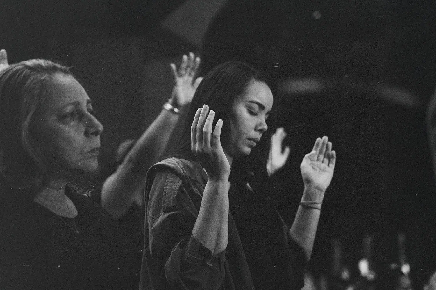 black and white photo of people with hands int he air praising
