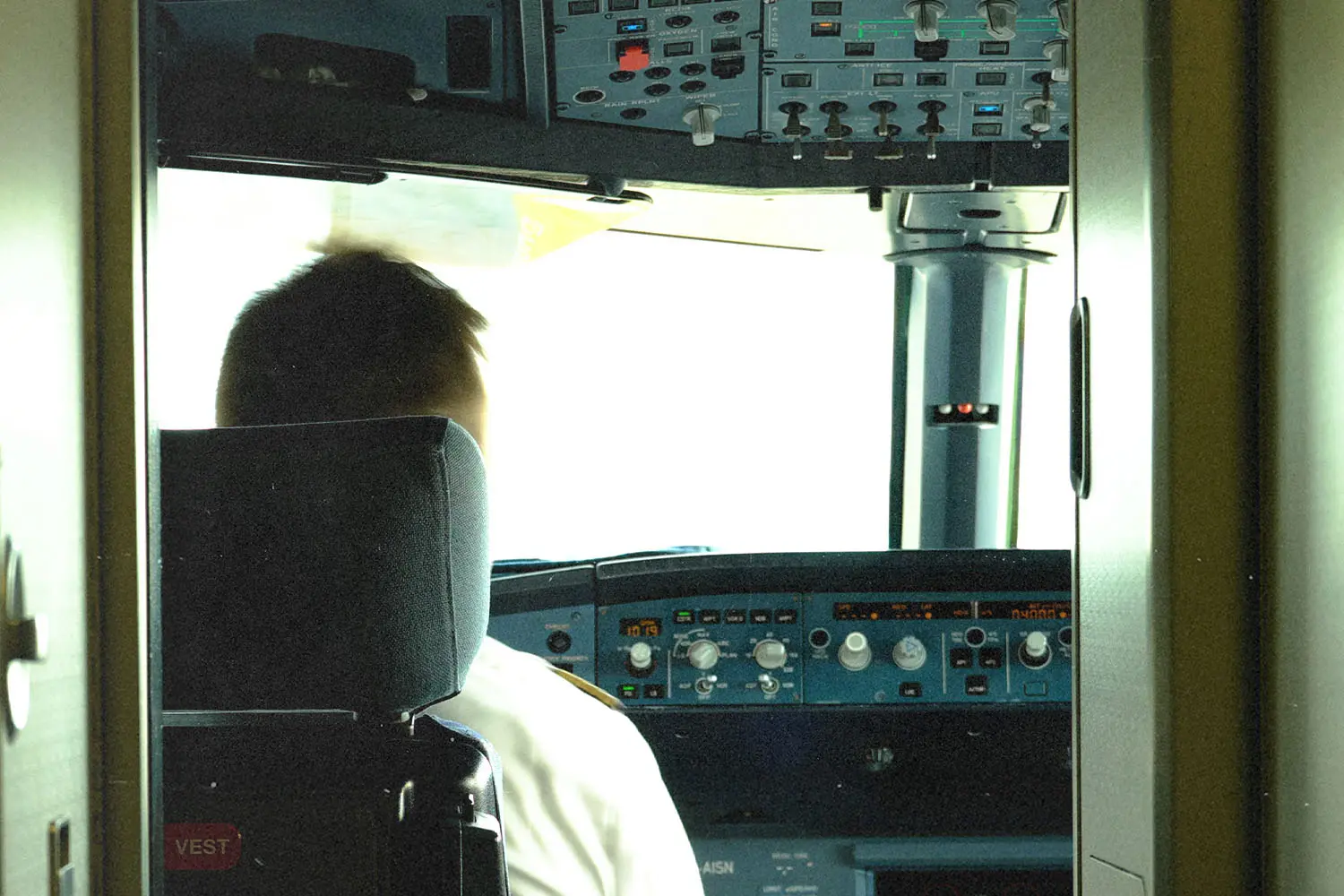 Back of the head of a pilot sitting at the head of the plane with controls