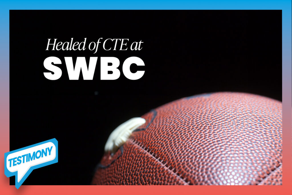 An American football player in full gear rests, bent over at the waist with hands on knees, hanging his head in exhaustion.