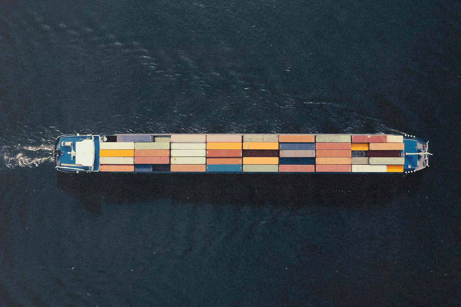 Aerial view of a long cargo ship carrying colorful shipping containers across dark water