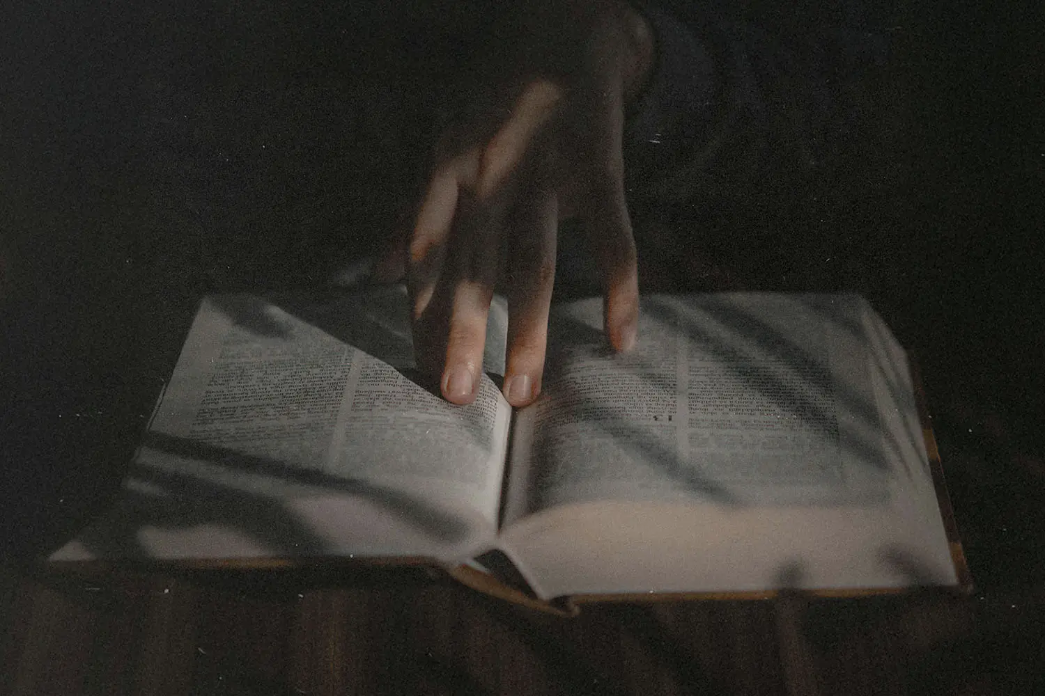Hand resting on the open pages of a book in low, moody light.