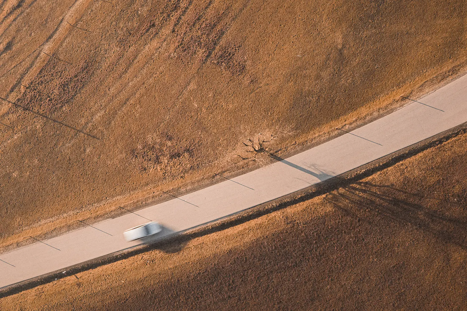 Blurred car driving on a open road with dry farm lands on both sides