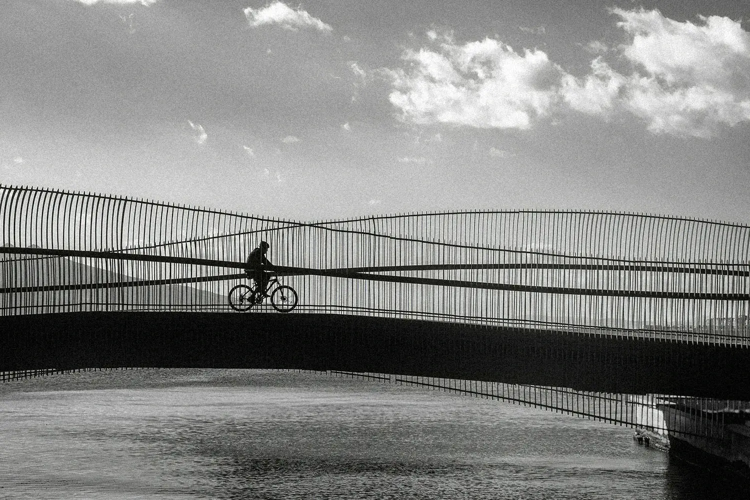 person on a bike riding over a bridge with water underneath