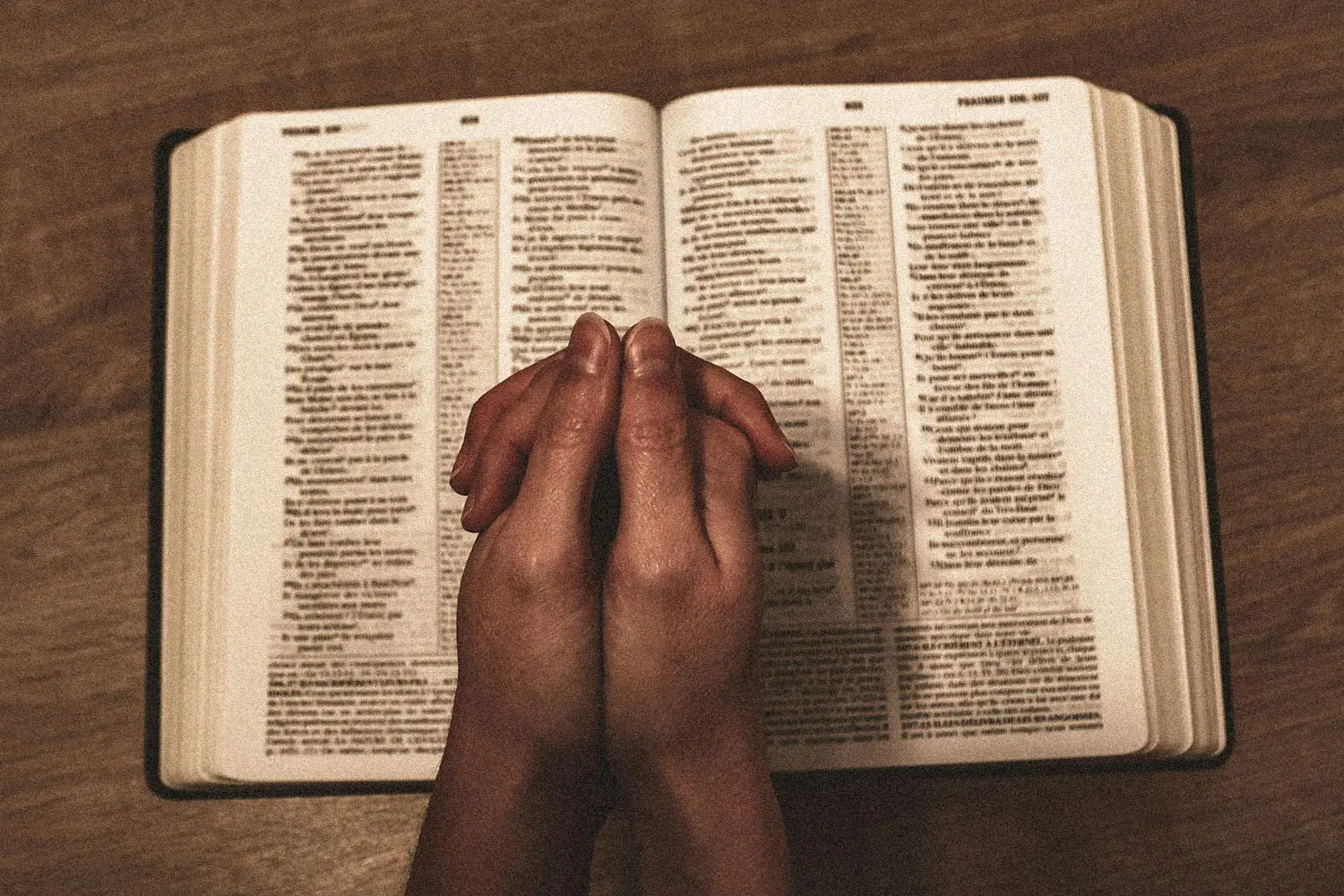 praying hands on top of an open bible