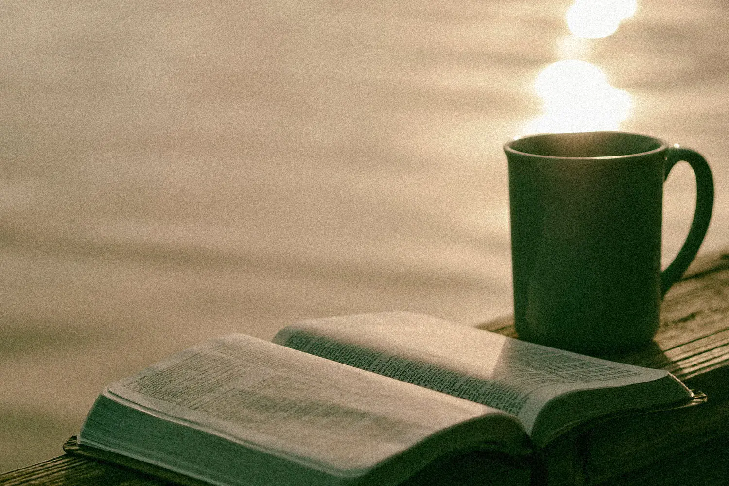 Coffee mug and open Bible on wooden ledge overlooking a body of water