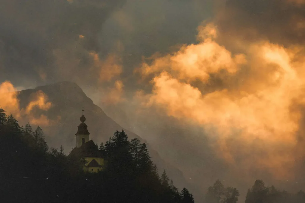 20240730-Consecration-of-the-Levitical-Priesthood-KCM-Blog - KCM Blog Cathedral peeking out from behind a tree line with a sunset in the sky