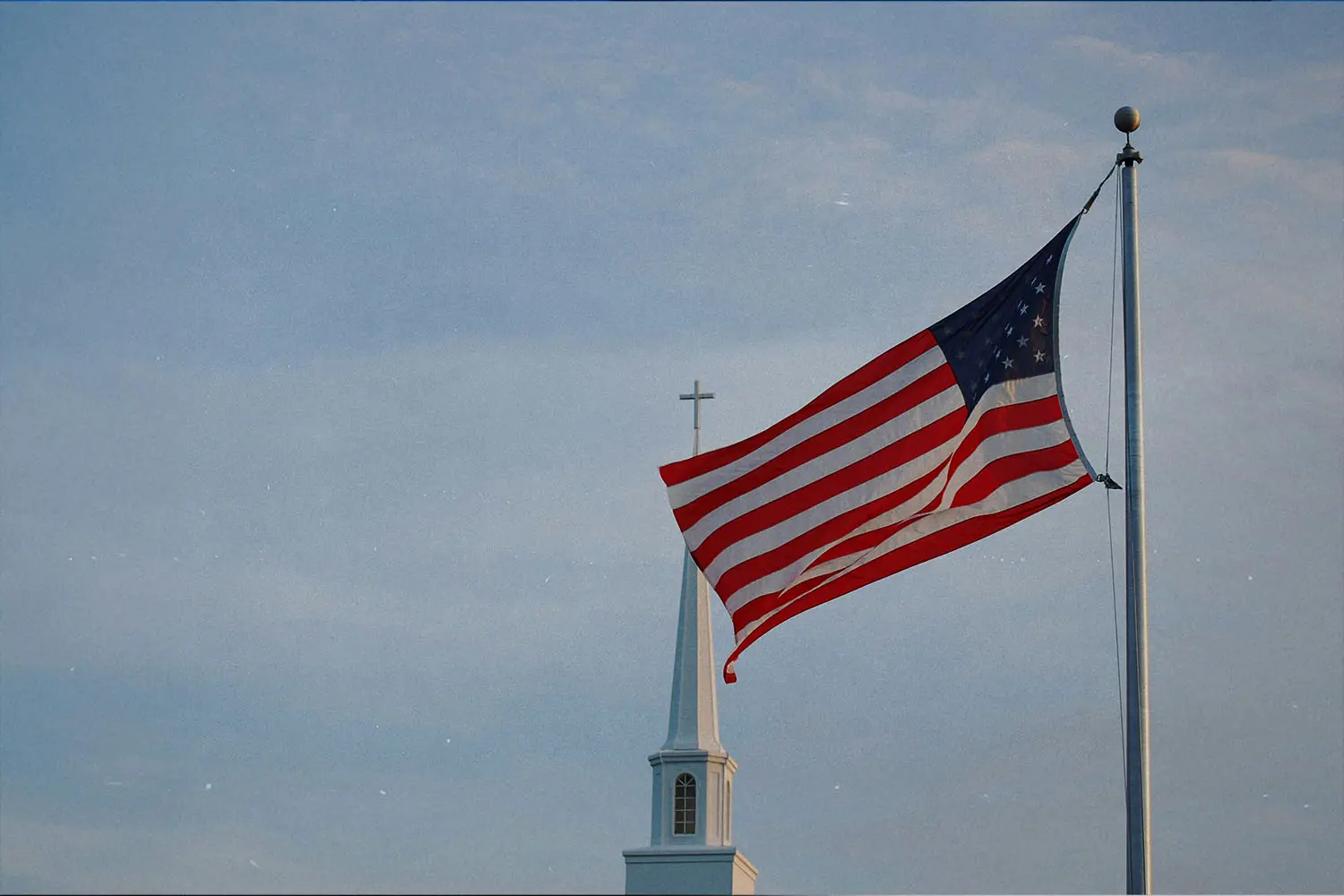 American flag flying on a pole in front of a church steeple