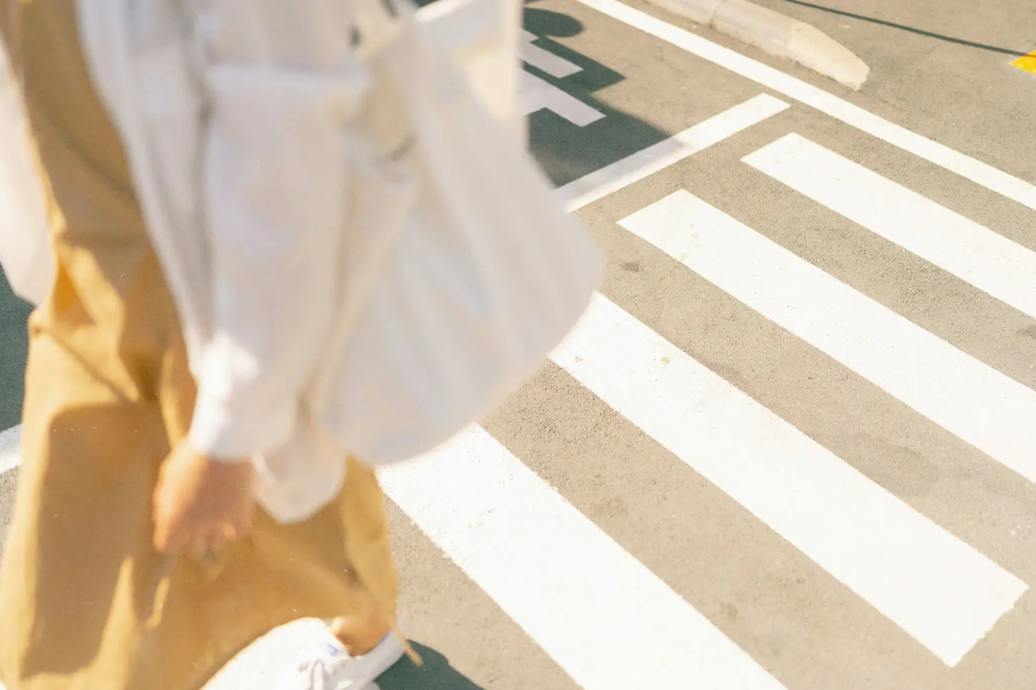 Person in a yellow dress and white jacket walking on a crosswalk