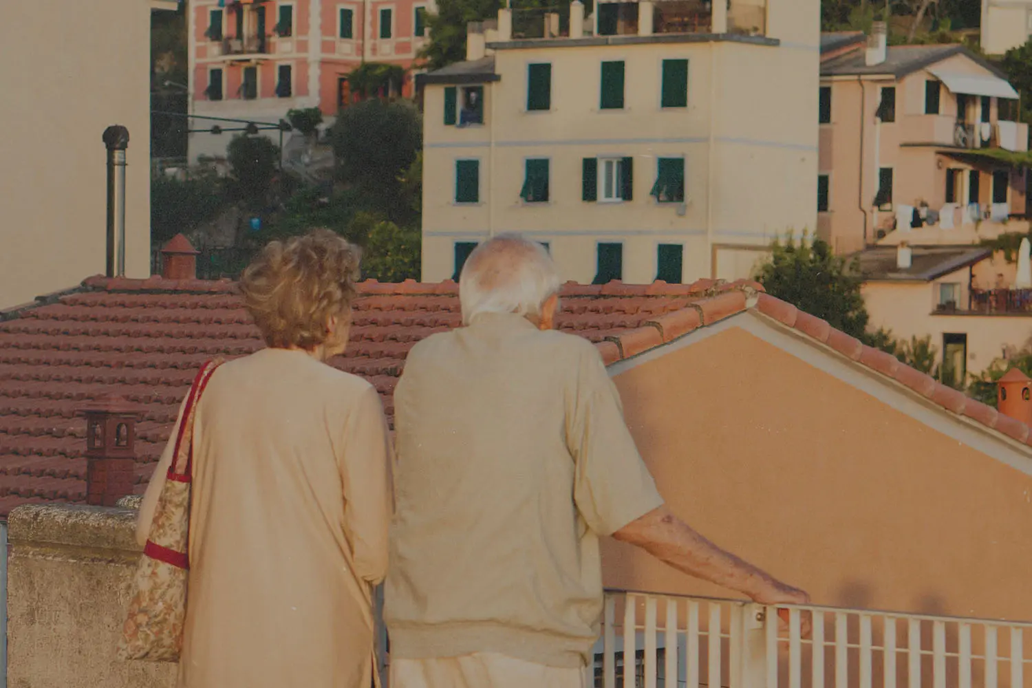 Back of an elderly couple standing on a balcony overlooking city buildings