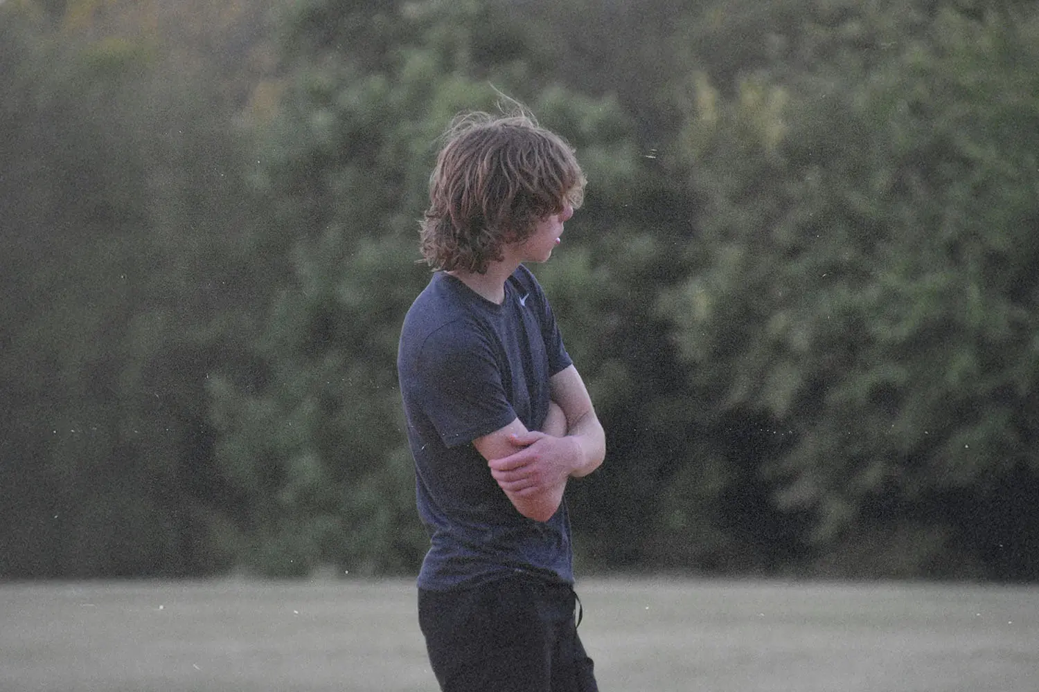 Teenage boy standing hunched with arms crossed looking away from the camera