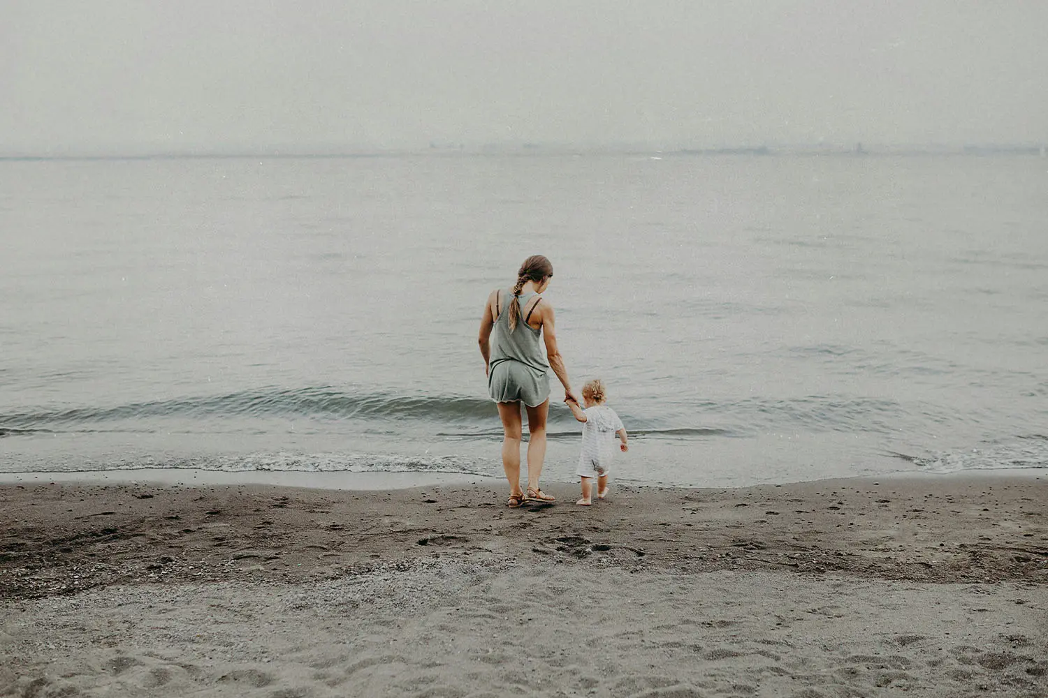 Mother walking on the shore with a child in hand into the sea