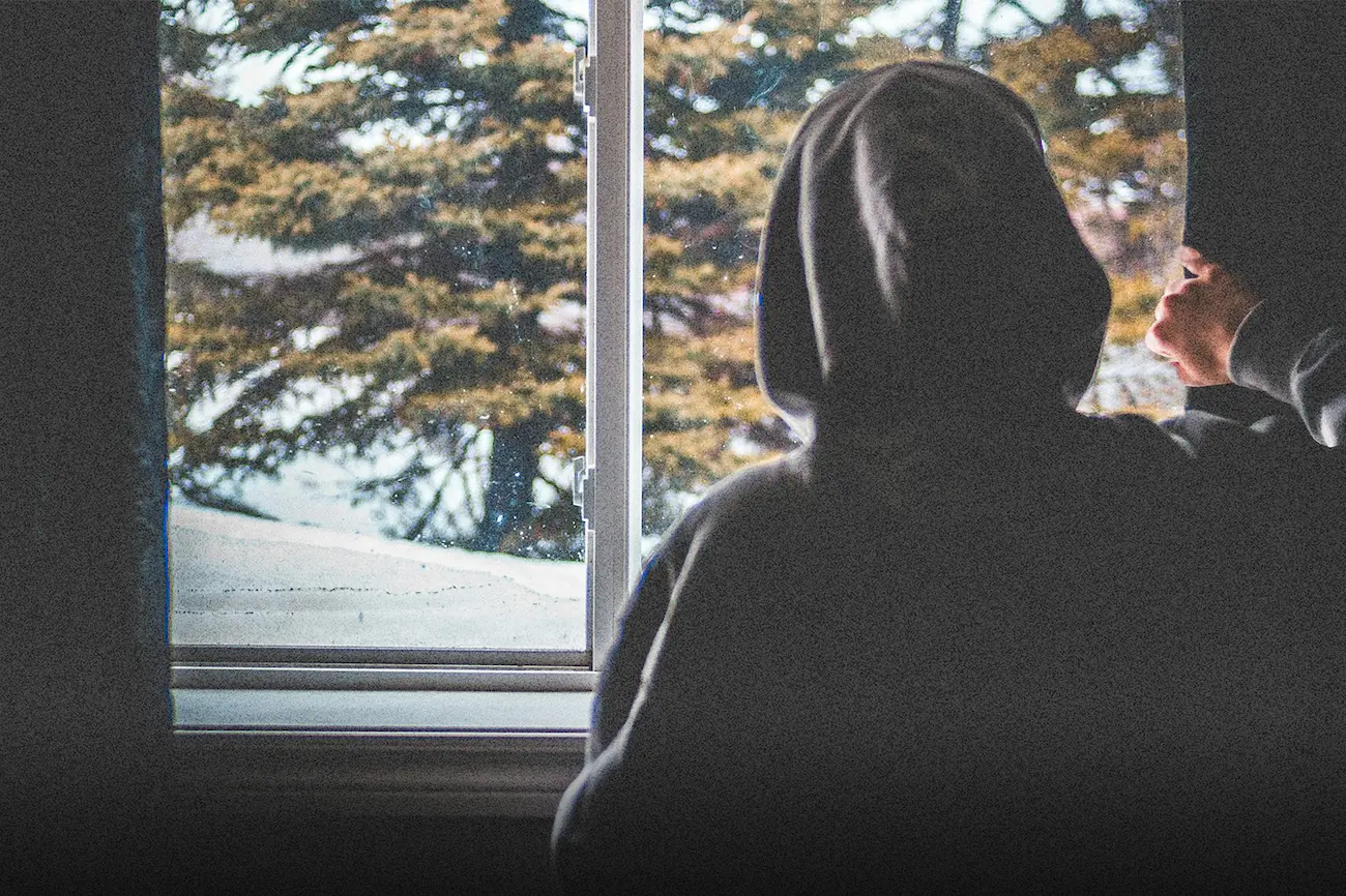 A person in a hoodie looks out a window on a cold day, reflecting on doubt and hope, symbolizing someone you love who may be questioning God in a hard season.